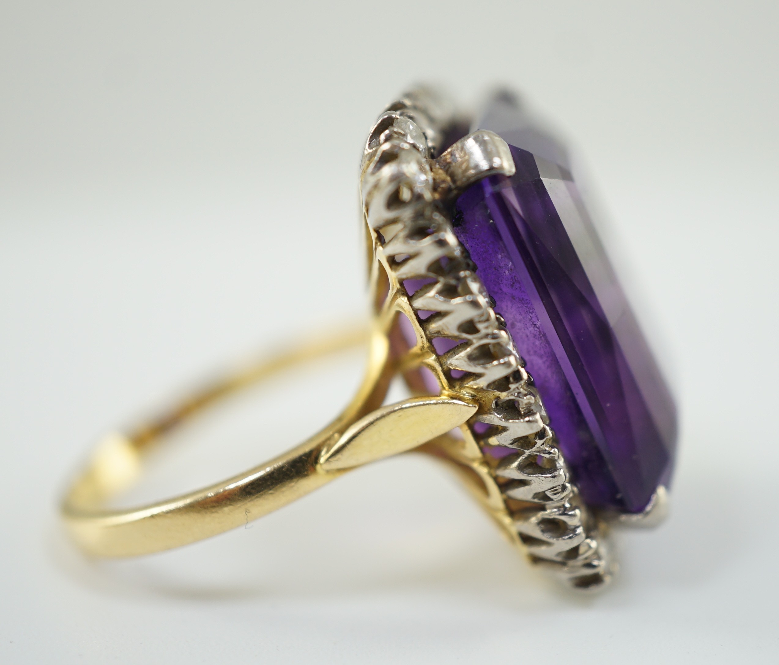 A large modern 18ct gold and emerald cut amethyst set dress ring, with diamond set border